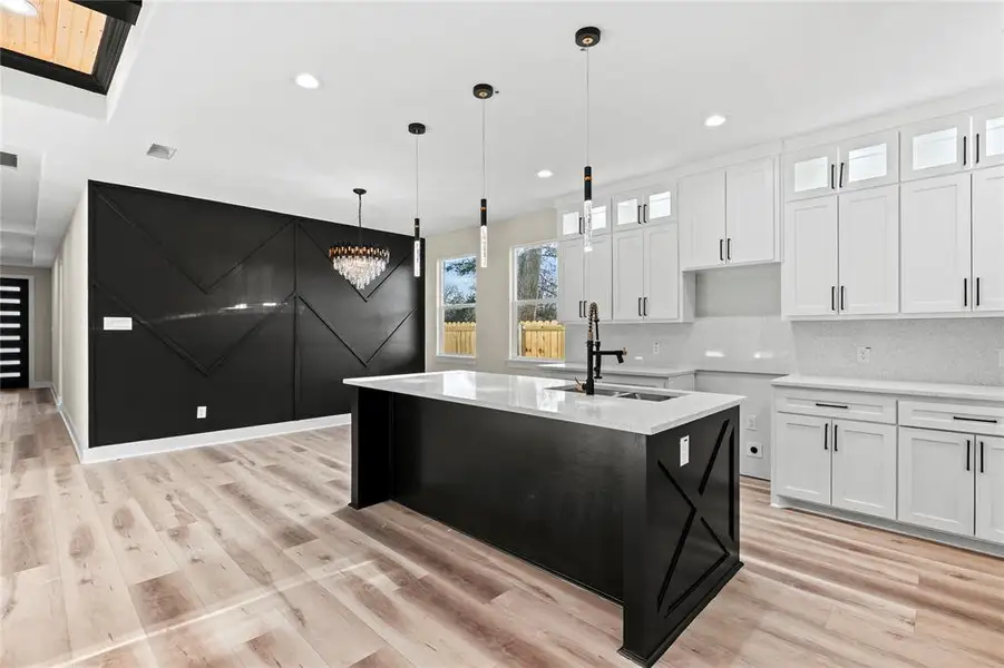 Kitchen with decorative light fixtures, white cabinetry, and an island with sink