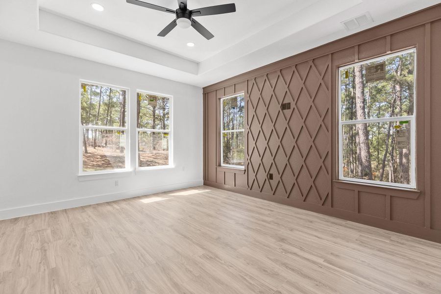 Empty room with a raised ceiling, ceiling fan, light wood-style flooring, and recessed lighting