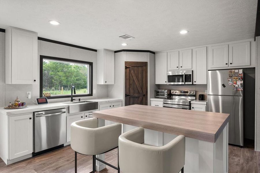 Modern kitchen featuring white shaker cabinetry, stainless steel appliances, a wood-finish island countertop, and wood-finish flooring Modern kitchen featuring white shaker cabinetry, stainless steel appliances, a wood-finish island countertop, and wood-finish flooring