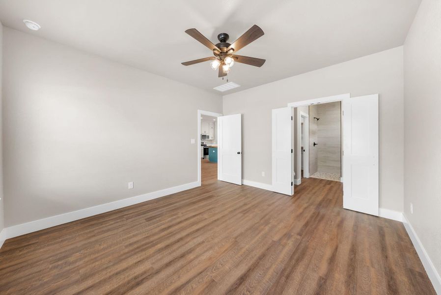 Unfurnished bedroom featuring ensuite bathroom, a ceiling fan, and dark wood-style floors