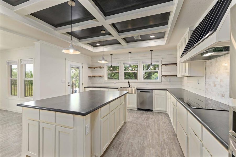 Spacious kitchen featuring a large island with storage cabinetry, dark countertops, white shaker-style perimeter cabinetry, stainless steel appliances, and a coffered ceiling with recessed lighting