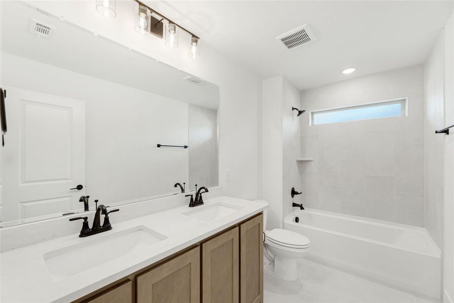 Bathroom with double sink vanity, white countertop, tub-shower combo, and large mirror with overhead lighting