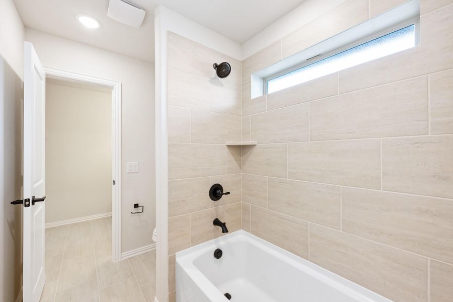 Bathroom with soaking tub, large tile surround, black fixtures, and a narrow window above the tub Bathroom with soaking tub, large tile surround, black fixtures, and a narrow window above the tub