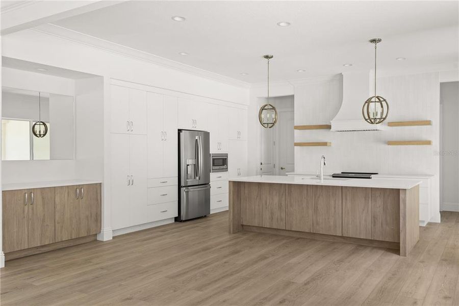 Open-concept kitchen showcasing white cabinetry, a center island with a contrasting light wood finish, stainless steel appliances, pendant lighting, and a seamless flow into the adjacent living spaces.