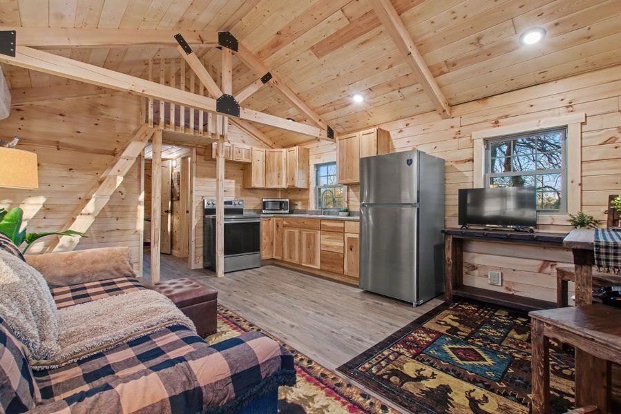 Kitchen featuring light brown cabinets, wood walls, a wooden ceiling with exposed beams, appliances with stainless steel finishes, and light wood-style floors