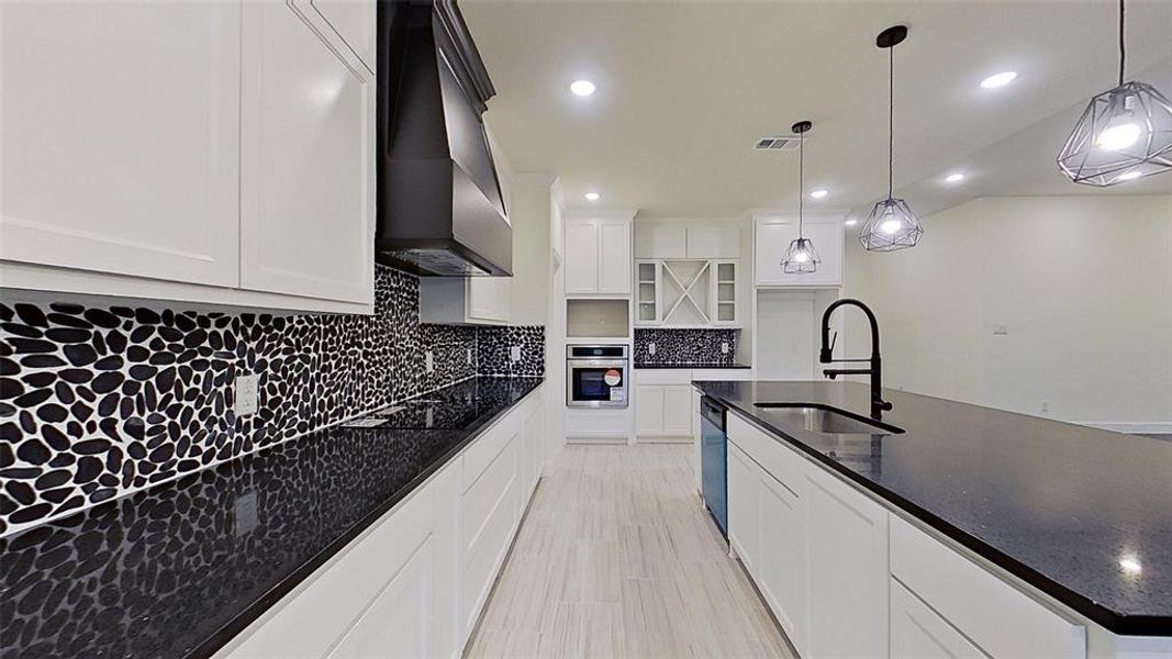 Kitchen with a large island with sink, stainless steel oven, white cabinets, dark stone counters, and tasteful backsplash Kitchen with a large island with sink, stainless steel oven, white cabinets, dark stone counters, and tasteful backsplash