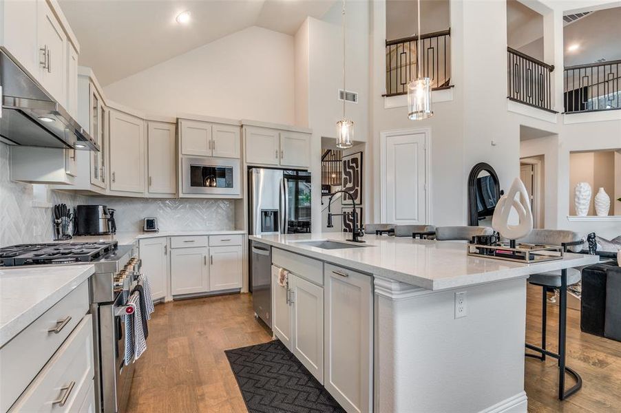 Kitchen with stainless steel appliances, light wood finished floors, a kitchen bar, pendant lighting, and high vaulted ceiling