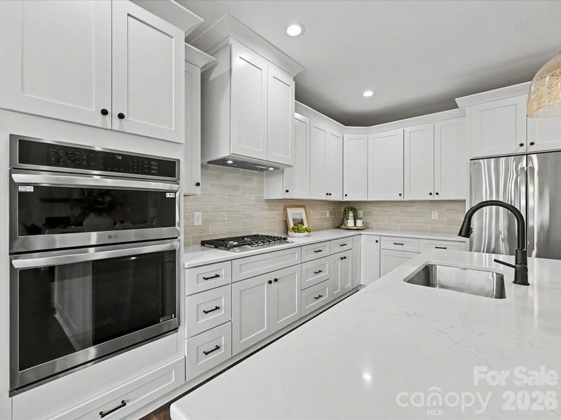 Bright and beautifully designed, this chef’s kitchen features quartz countertops, custom white cabinetry, stainless steel appliances, and a large center island overlooking the open-concept living space.