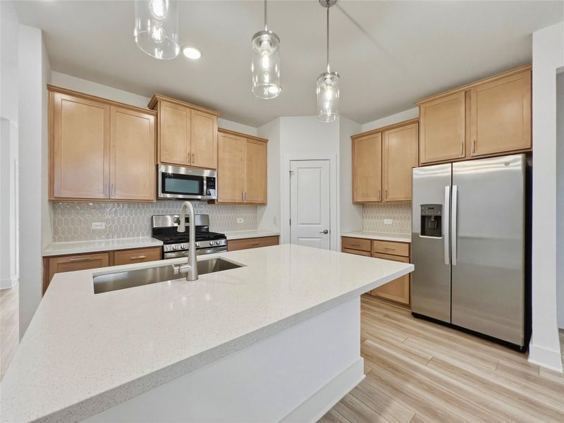 Kitchen with stainless steel appliances, light stone counters, light wood-type flooring, hanging light fixtures, and tasteful backsplash