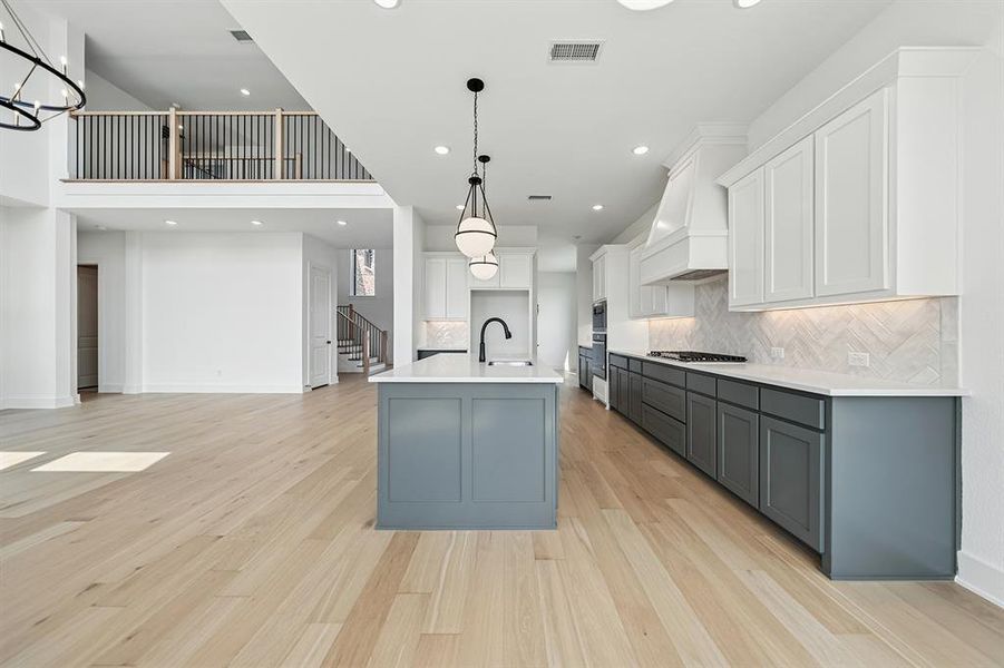 Kitchen featuring white cabinets, gray cabinetry, an island with sink, hanging light fixtures, and recessed lighting