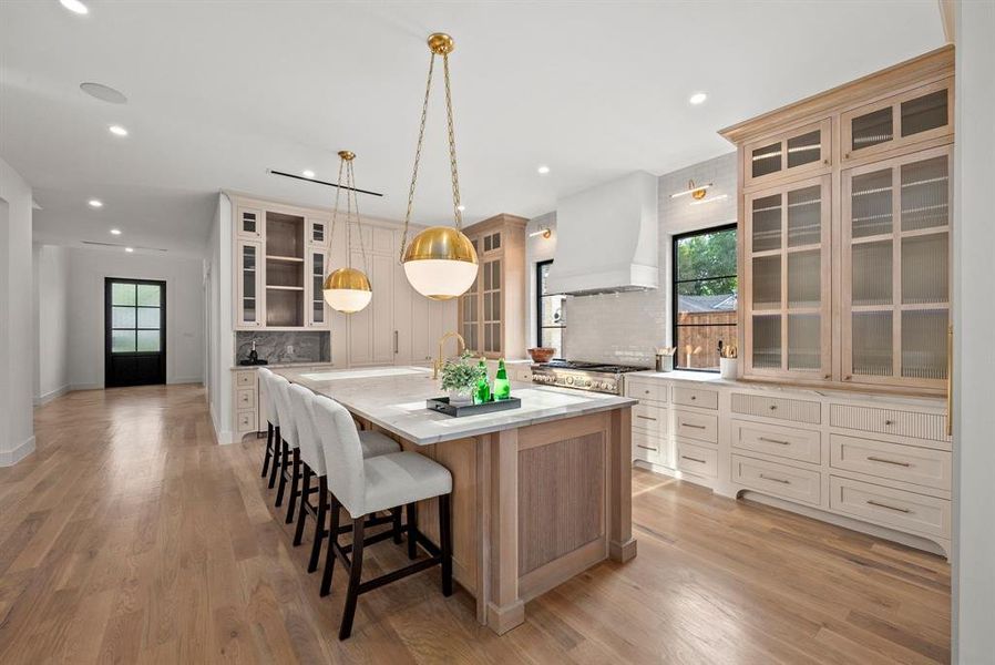 The kitchen features hardwood floors, a large island with a marble countertop, and custom cabinetry with glass-front uppers