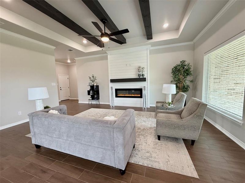 Living room featuring beam ceiling, a glass covered fireplace, wood finished floors, crown molding, and recessed lighting Living room featuring beam ceiling, a glass covered fireplace, wood finished floors, crown molding, and recessed lighting