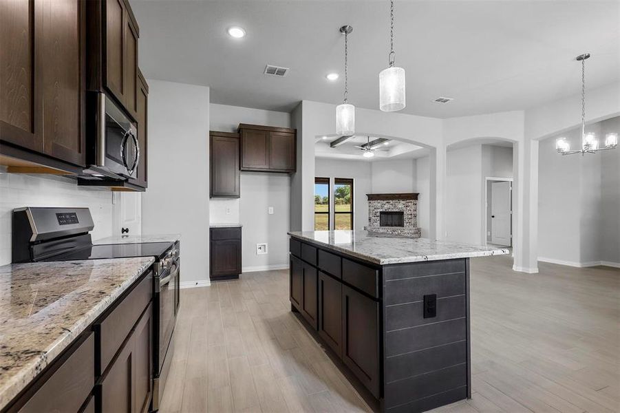 Kitchen featuring a stone fireplace, appliances with stainless steel finishes, light wood-type flooring, and a kitchen island