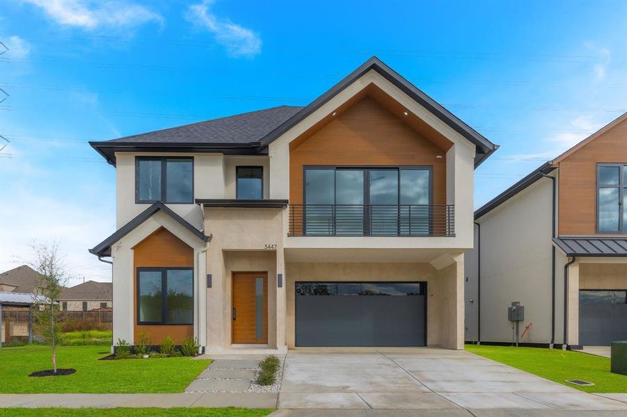 Contemporary home with a balcony, a front lawn, driveway, stucco siding, and an attached garage