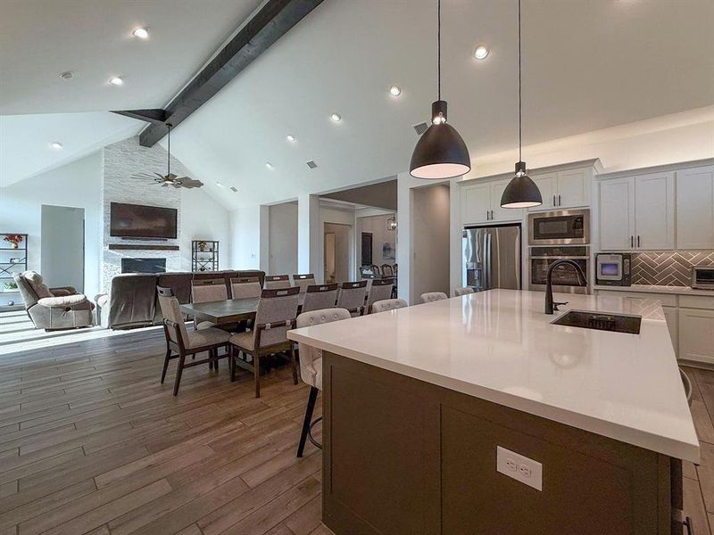 Kitchen with beamed ceiling, a kitchen breakfast bar, an island with sink, a stone fireplace, and decorative light fixtures Kitchen with beamed ceiling, a kitchen breakfast bar, an island with sink, a stone fireplace, and decorative light fixtures