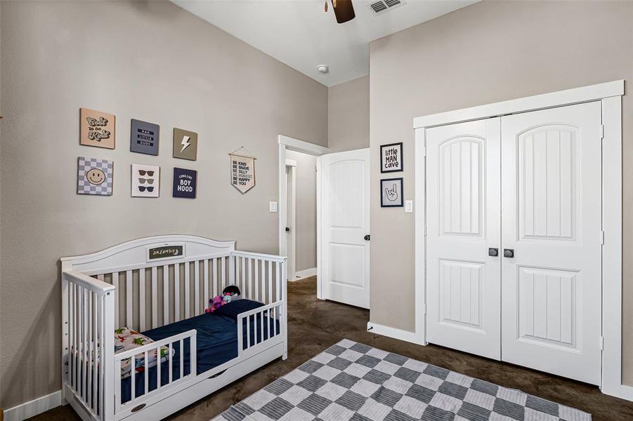 Bedroom with ceiling fan, a crib, a closet, and concrete flooring Bedroom with ceiling fan, a crib, a closet, and concrete flooring