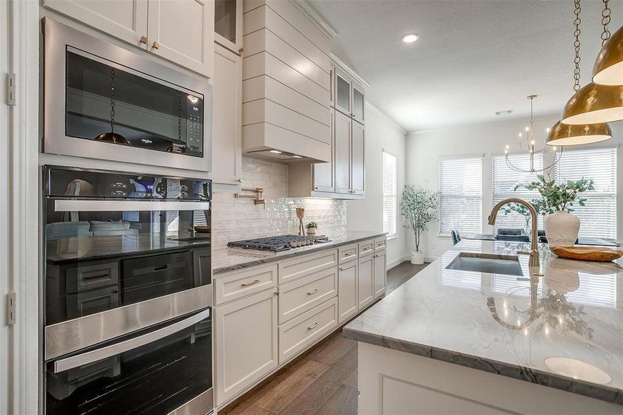 Kitchen featuring a large island, Quartzite countertops, gold hardware, decorative light fixtures, custom cabinetry to the ceiling, gas cooktop, double oven and walk in pantry