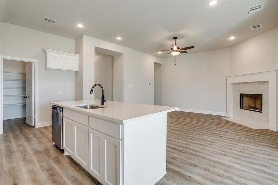 Kitchen featuring sink, light hardwood / wood-style floors, a kitchen island with sink, a fireplace, and white cabinets