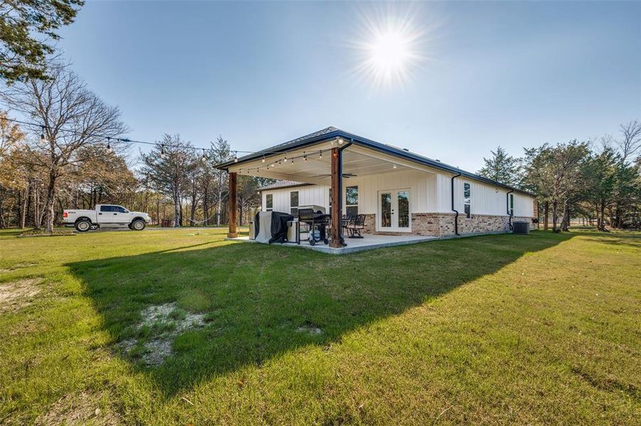 Rear view of property featuring a yard, french doors, a patio, brick siding, and board and batten siding