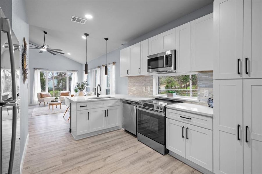 Kitchen with stainless steel appliances, white cabinets, vaulted ceiling, a peninsula, and pendant lighting Kitchen with stainless steel appliances, white cabinets, vaulted ceiling, a peninsula, and pendant lighting