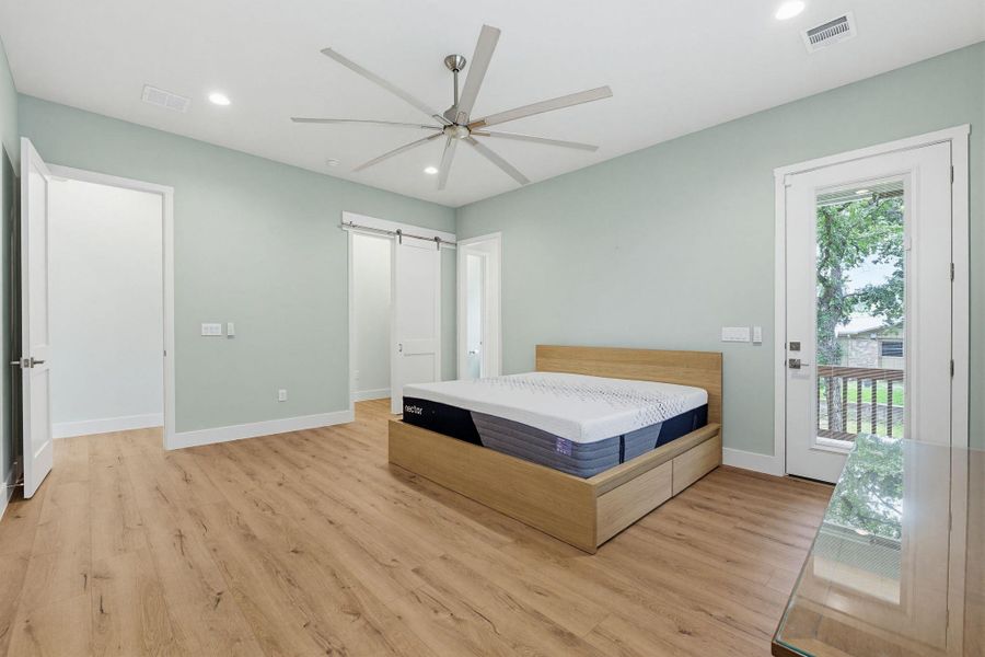 A spacious sleeping area with light hardwood floors and a door leading to a balcony.