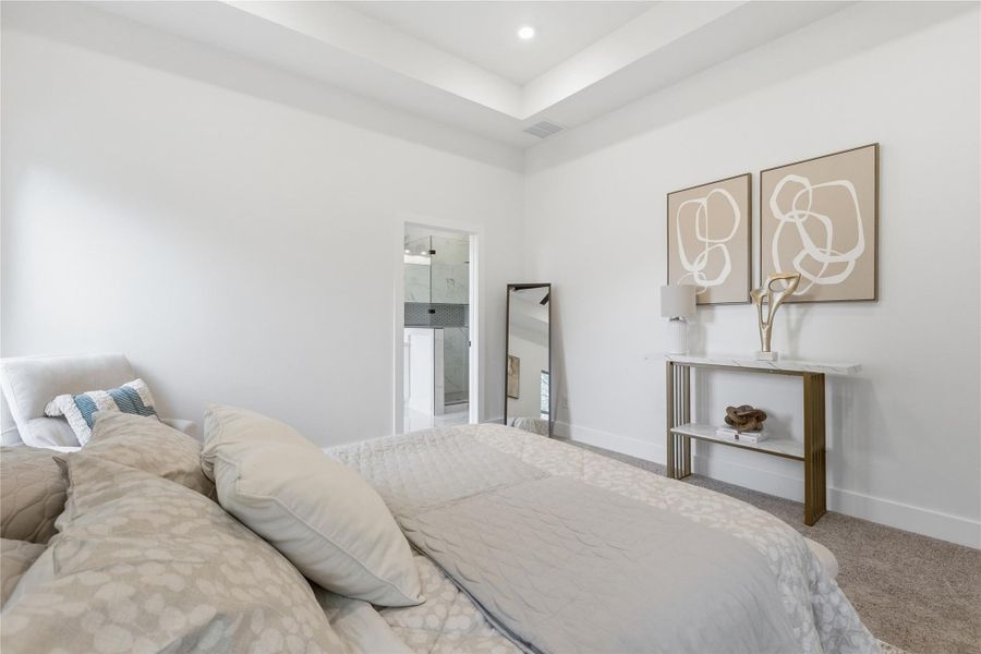 Carpeted bedroom featuring a raised ceiling and ensuite bath