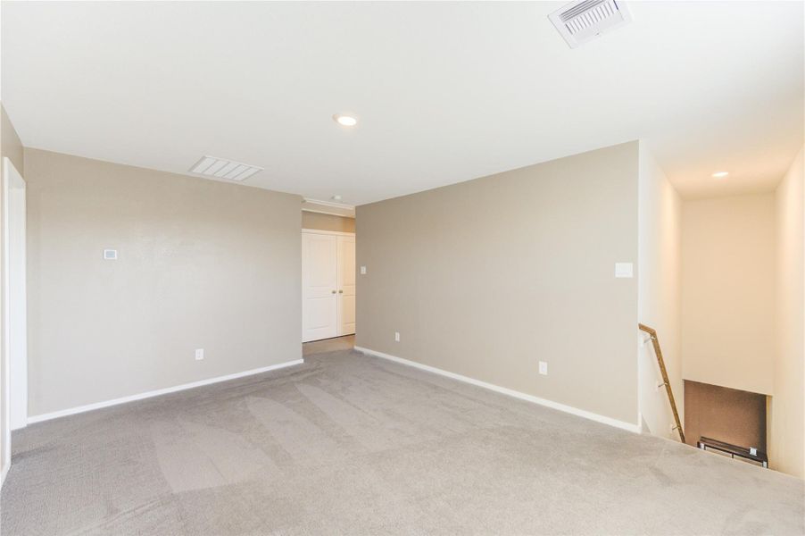 This photo showcases a bright, open room with neutral walls and carpet flooring. It features recessed lighting, a small stairway leading down, and a double-door closet, offering a versatile space for various uses.