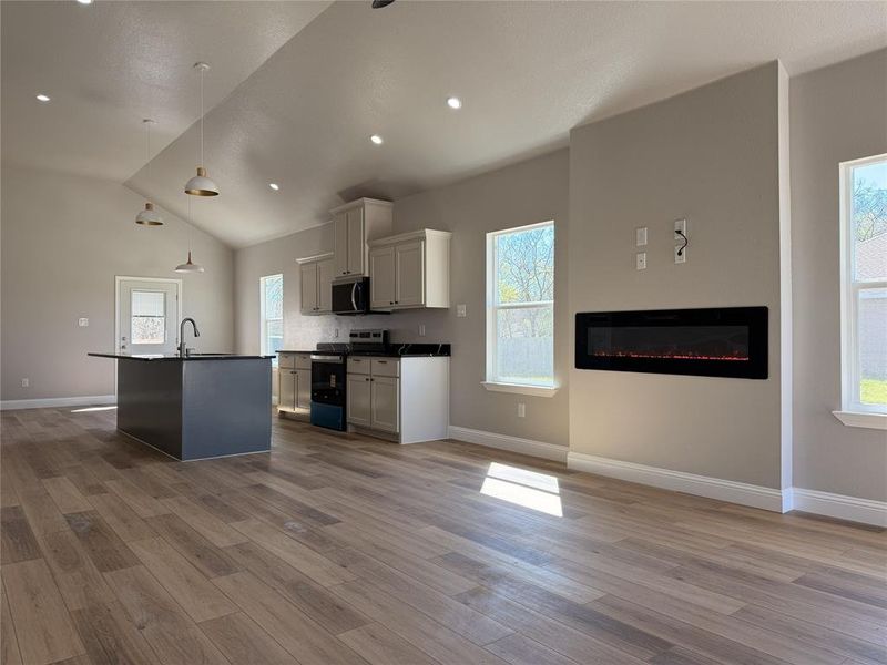 Kitchen with dark countertops, stainless steel appliances, open floor plan, a glass covered fireplace, and decorative light fixtures