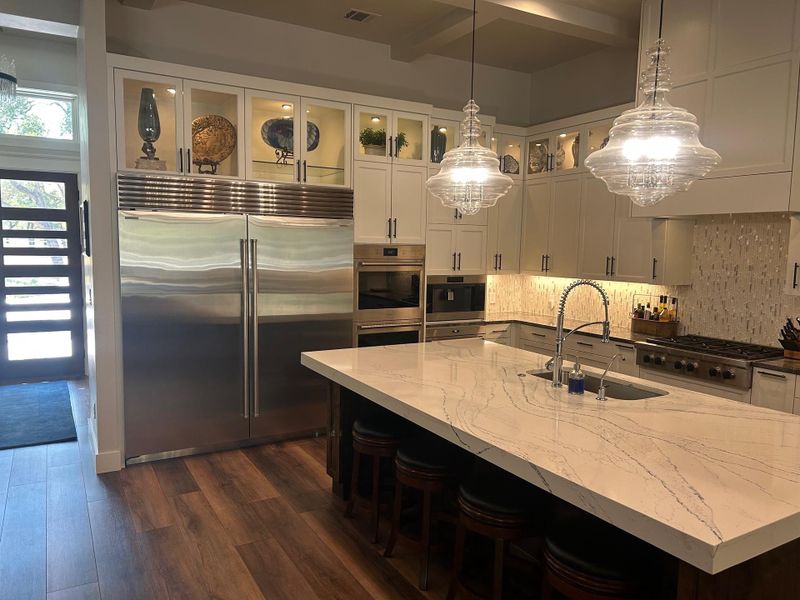 Kitchen featuring stainless steel appliances, a breakfast bar area, pendant lighting, glass insert cabinets, and white cabinetry Kitchen featuring stainless steel appliances, a breakfast bar area, pendant lighting, glass insert cabinets, and white cabinetry