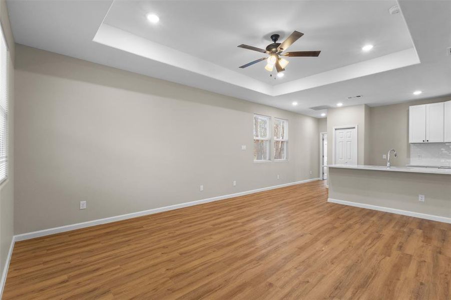 Unfurnished living room with a raised ceiling, light wood-type flooring, recessed lighting, and a ceiling fan