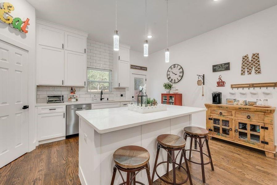 Kitchen featuring a breakfast bar area, a kitchen island, dark wood-type flooring, tasteful backsplash, and decorative light fixtures