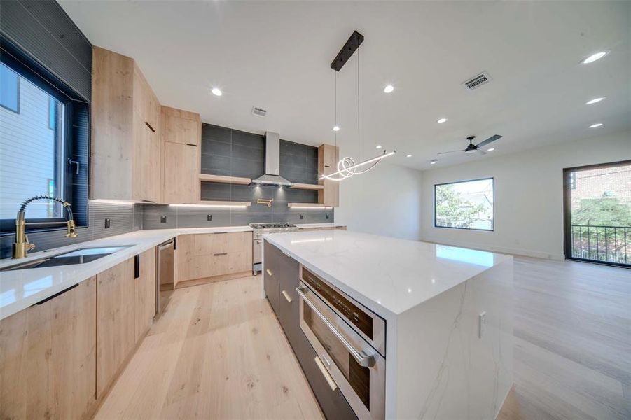 Kitchen featuring light stone countertops, sink, hanging light fixtures, range hood, and a kitchen island