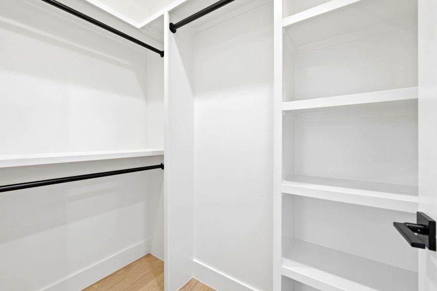 Custom closet system with multiple hanging rods, integrated shelving units, and wood-finish flooring
