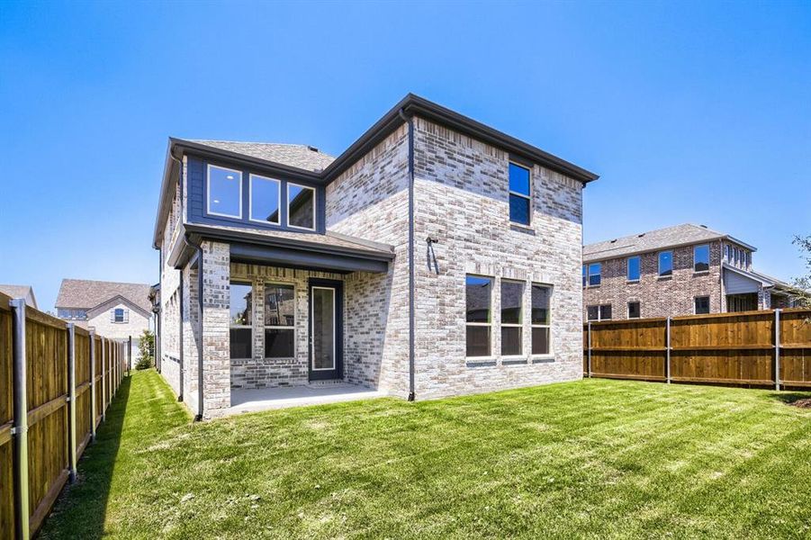 Rear exterior featuring a covered patio with brick columns, a manicured lawn, and a privacy fence