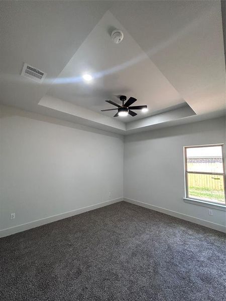 Bedroom with a raised ceiling, dark carpet, a ceiling fan, and a smoke detector Bedroom with a raised ceiling, dark carpet, a ceiling fan, and a smoke detector