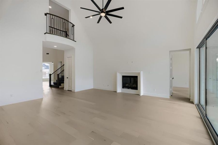 Spacious living area featuring high vaulted ceilings, light wood-finish flooring, and a modern fireplace with a white surround Spacious living area featuring high vaulted ceilings, light wood-finish flooring, and a modern fireplace with a white surround