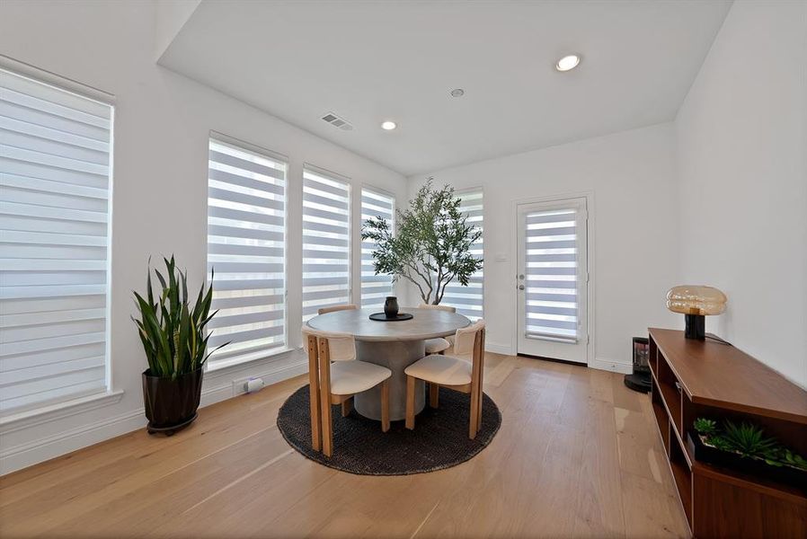 Bright interior space featuring light wood-finish flooring, recessed lighting, and multiple windows with horizontal blinds