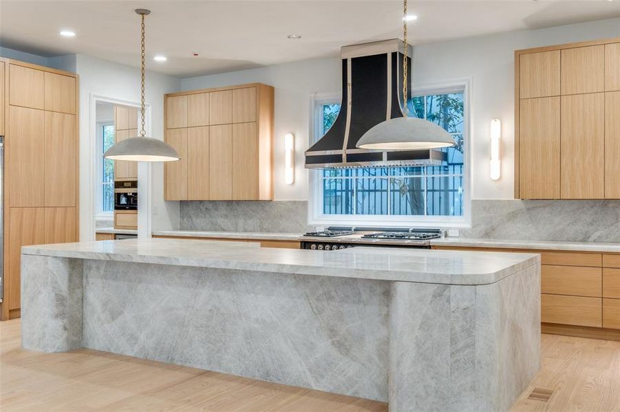 Kitchen featuring stainless steel gas stovetop, island range hood, a spacious island, light brown cabinetry, and light hardwood / wood-style floors