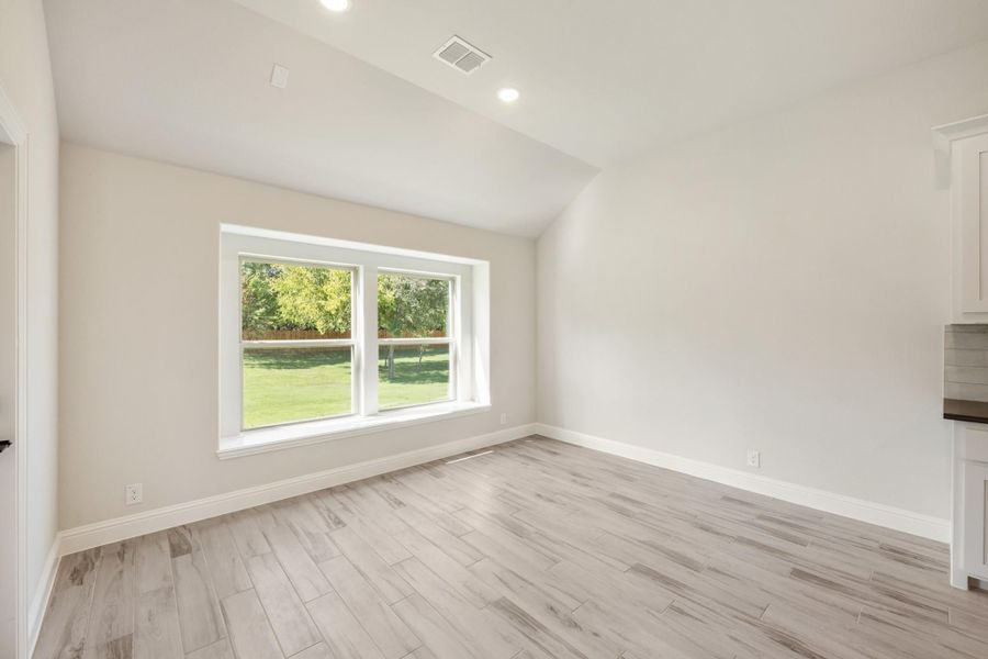 Empty room with vaulted ceiling, light wood floors, and large window overlooking a green yard