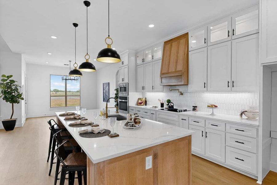 Kitchen featuring light wood-type flooring, an island with sink, backsplash, recessed lighting, and light stone counters