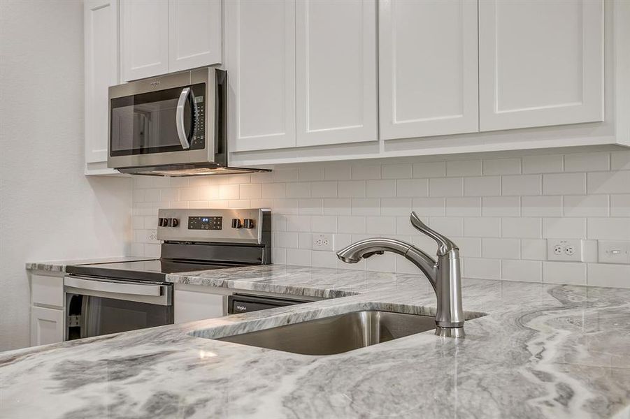 Kitchen featuring white cabinetry, stainless steel appliances, and light stone countertops