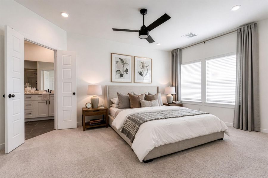 Retreat to this generously sized primary suite featuring plush carpeting, soft neutral tones, and abundant natural light streaming through large windows. The spacious layout easily accommodates oversized furniture, while the modern ceiling fan adds both comfort and style. With direct access to the ensuite bath, this serene bedroom offers the perfect balance of relaxation and functionality. This photo is virtually staged.