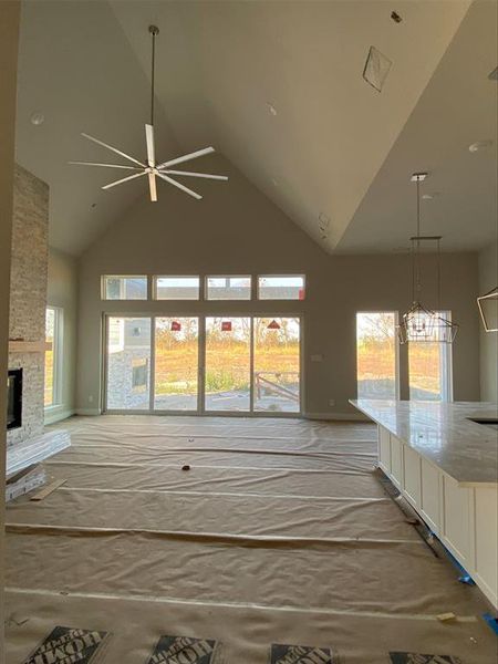 Unfurnished living room featuring high vaulted ceiling, a stone fireplace, a ceiling fan, and healthy amount of natural light Unfurnished living room featuring high vaulted ceiling, a stone fireplace, a ceiling fan, and healthy amount of natural light
