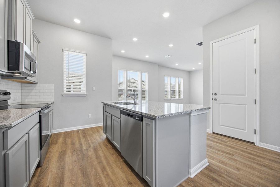 Kitchen featuring appliances with stainless steel finishes, light stone counters, a center island with sink, light wood-style flooring, and gray cabinets
