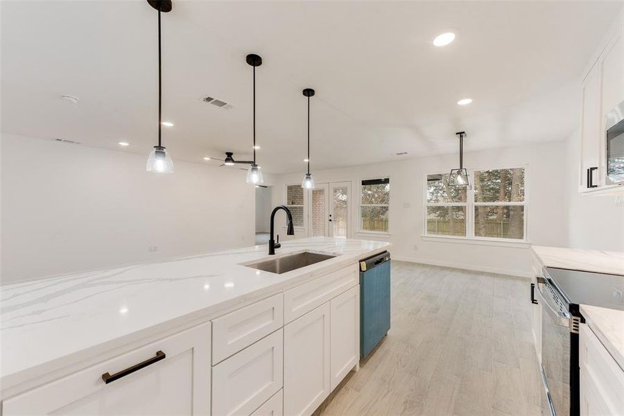 Kitchen featuring appliances with stainless steel finishes, pendant lighting, white cabinetry, sink, and light stone counters