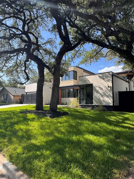A modern architectural marvel stands behind mature, graceful trees, presenting an inviting curb appeal.