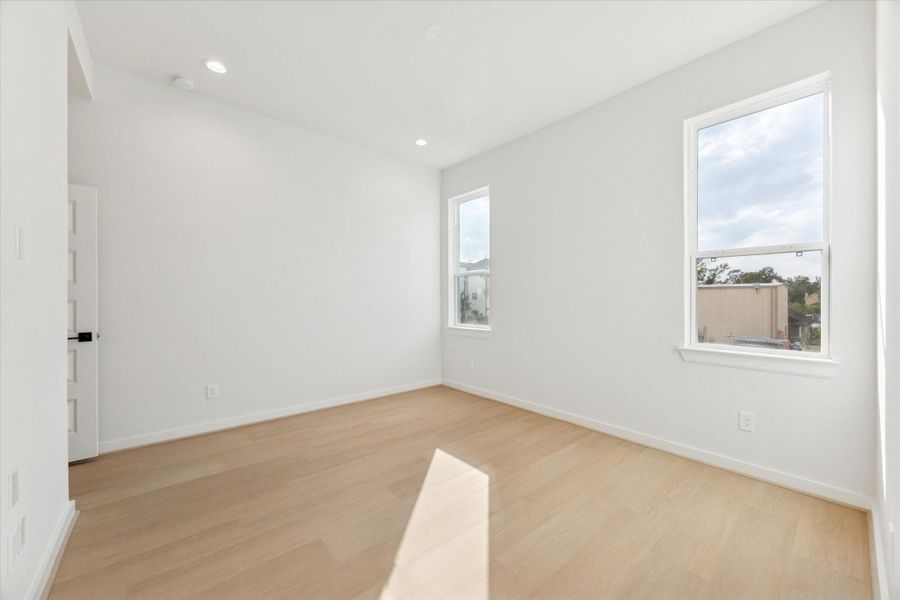 Another view of the primary bedroom showcases its warm tones, soaring ceilings, and natural light, emphasizing the serene and luxurious retreat-like atmosphere.