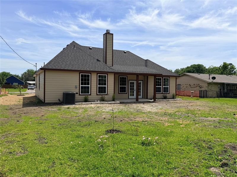 Rear exterior featuring a covered patio, multiple double-hung windows, and a prominent chimney structure