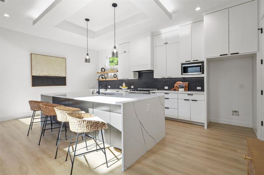 Kitchen with light hardwood / wood-style floors, white cabinetry, a kitchen island with sink, and stainless steel microwave