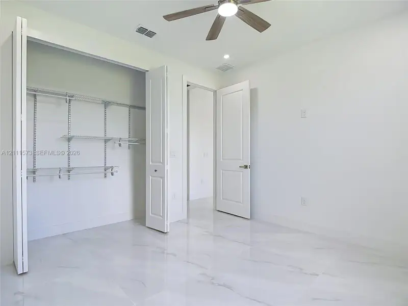 Large-format tile flooring, multi-panel doors, ceiling fan with integrated lighting, and built-in closet shelving